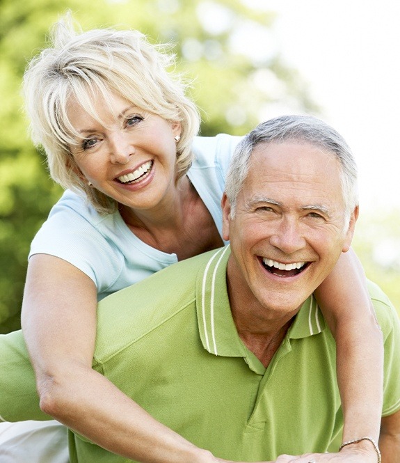 Older man and woman with dentures smiling together outdoors
