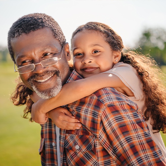 Grandfather and granddaughter smiling after family dentistry