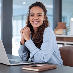 a happy woman sitting at a desk with her laptop