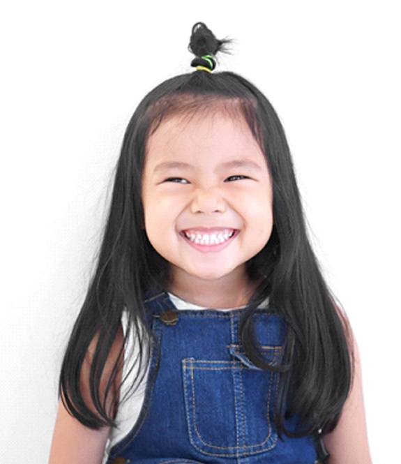 A little girl wearing a denim jumper and showing off her healthy, beautiful smile after seeing her dentist in Lancaster