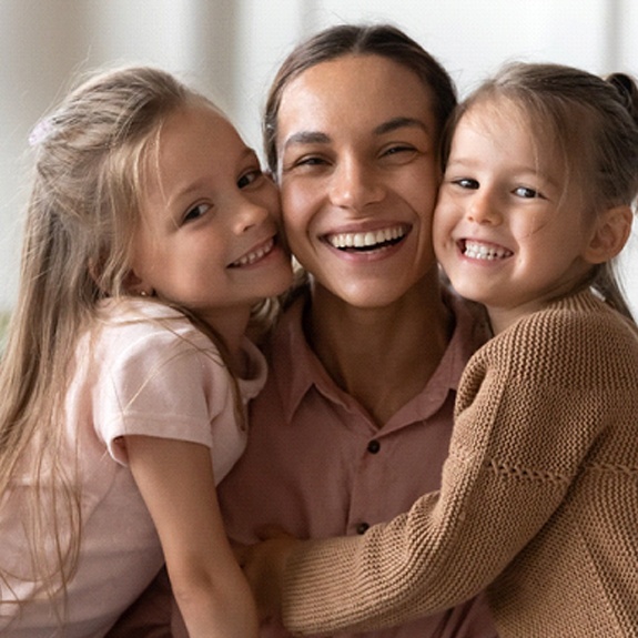 A mother and her two daughters showing off their healthy smiles