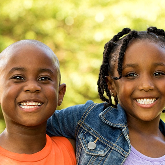 A young boy and girl hugging and smiling after seeing their dentist for fluoride treatments