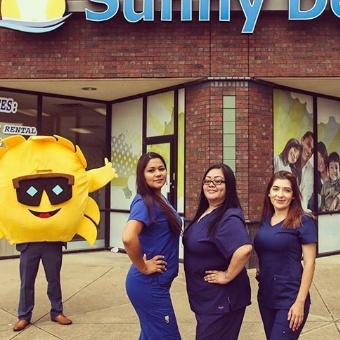 Three team members and sun mascot in front of dental office