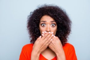 woman in orange shirt covering her mouth