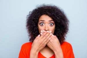 woman in orange shirt covering her mouth 