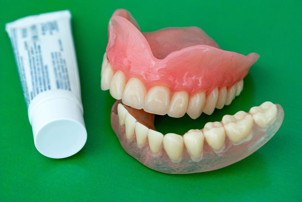 Dentures on green surface next to tube of cream