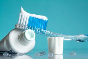 Toothbrush on open tube of toothpaste next to cap with water droplets